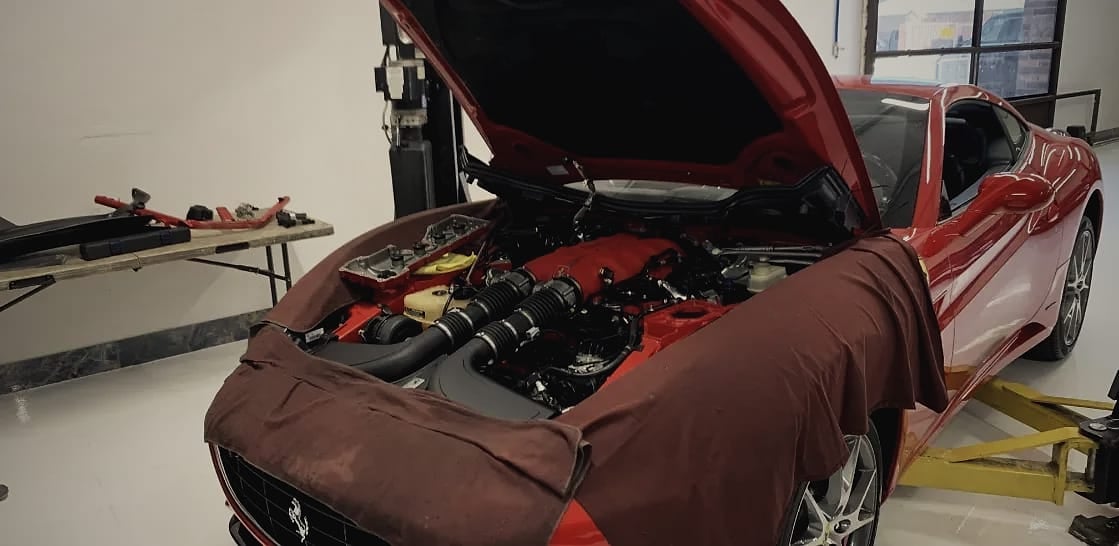 A red Ferrari California on a lift with its bonnet open and a fender cover over the front, showing the V8.