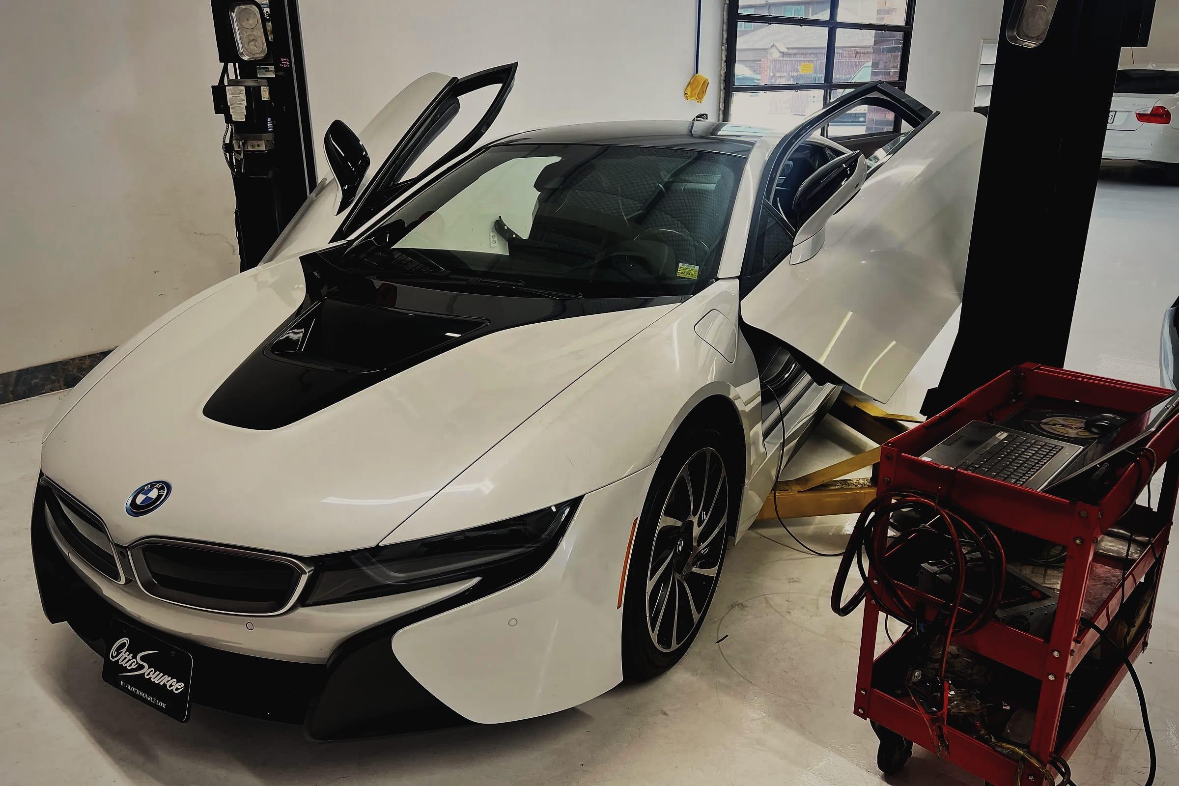 A white BMW i8 with its doors and bonnet open between the lift posts, next to a red tool cart.
