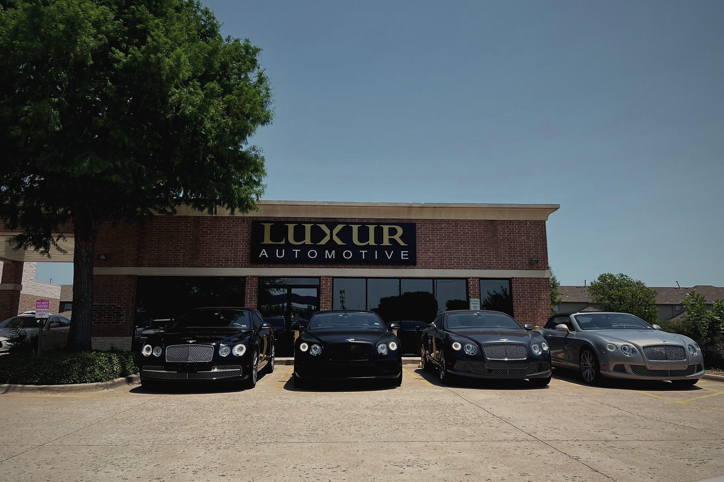 Four Bentleys parked side by side in front of the Luxur Automotive building.