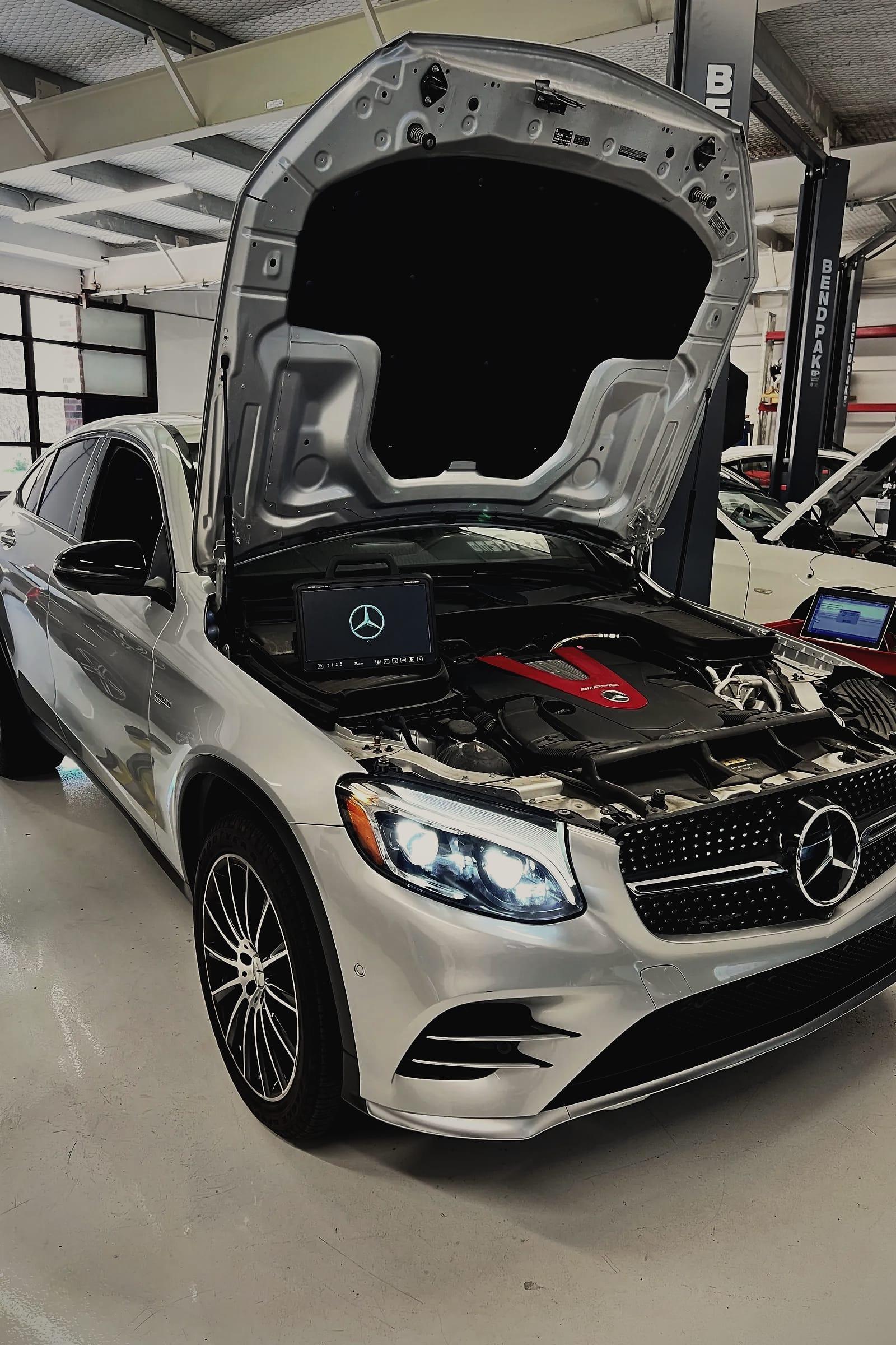 A silver Mercedes-Benz GLC Coupe with its bonnet open and a Mercedes diagnostic tablet resting in the engine bay.