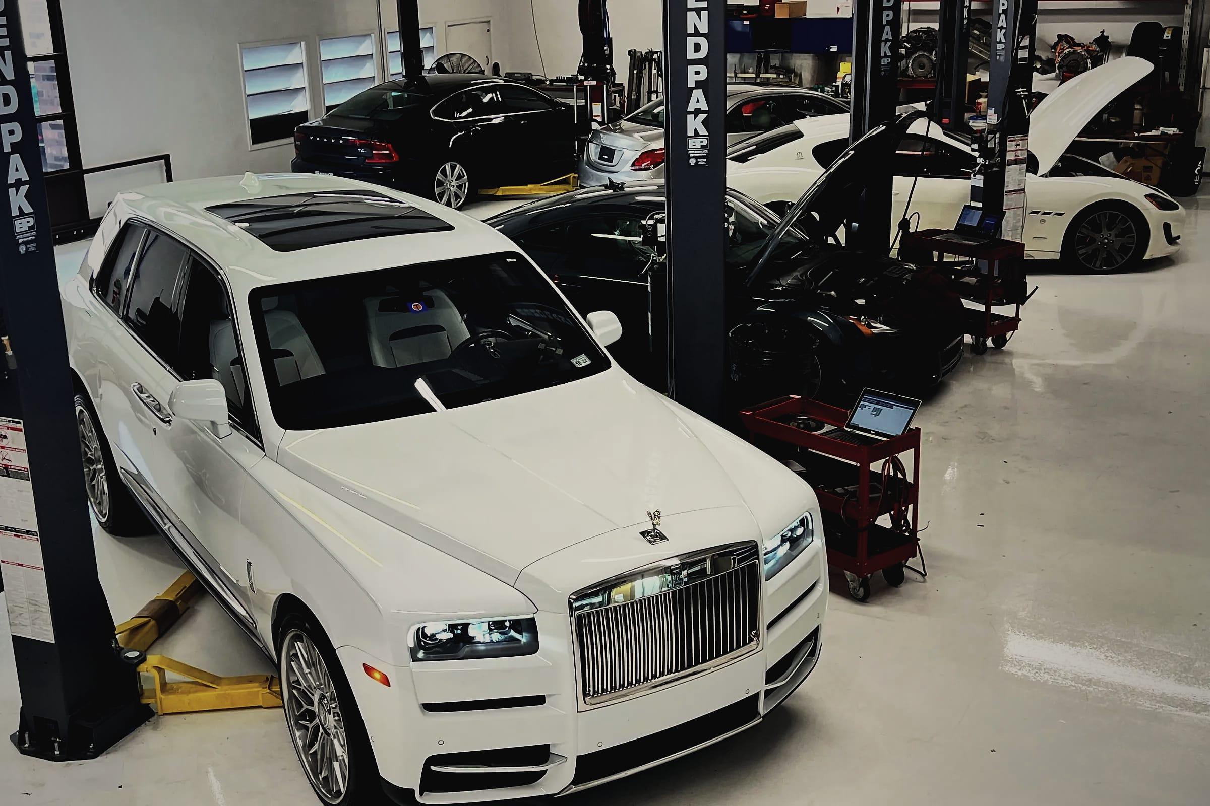 A white Rolls-Royce Cullinan between the lifts, with a Maserati GranTurismo and other cars being worked on behind it.