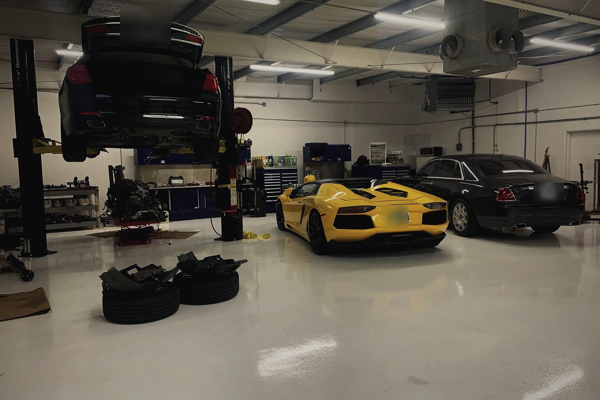 The workshop floor: a black saloon raised on a lift, an engine out of a car on a stand, a yellow Lamborghini Aventador Roadster and a black Rolls-Royce Ghost.